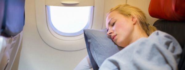 Frau schläft auf einem Kopfkissen im Flugzeug