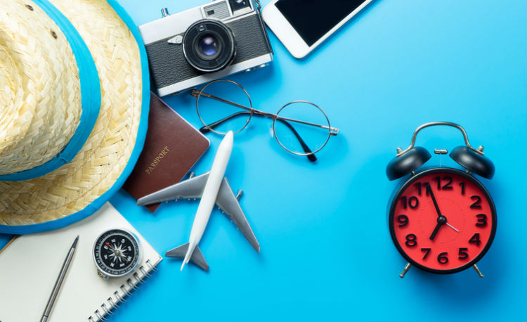 Reisepass und weitere Reiseaccessoires die neben einer Uhr auf einem Tisch liegen