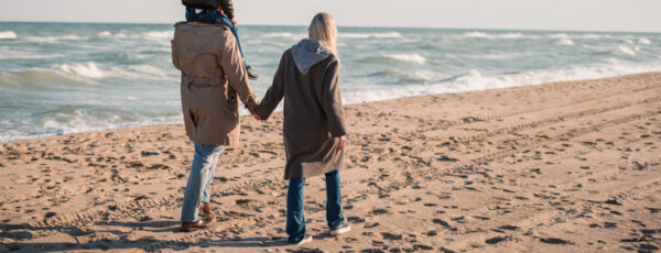 back view of parents with son on shoulders walking on seashore in autumn