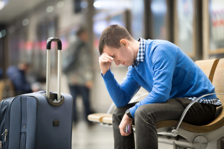 Junger, müder Mann sitzt mit Gepäck am Flughafen