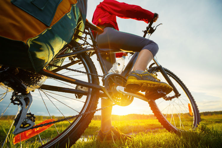 Fahrradfahrerin mit bepacktem Trekkingrad im Sonnenuntergang